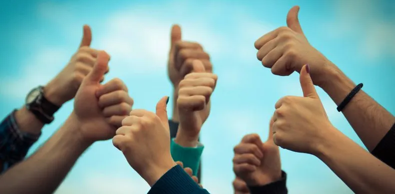 Group of diverse hands giving thumbs up against a blue sky